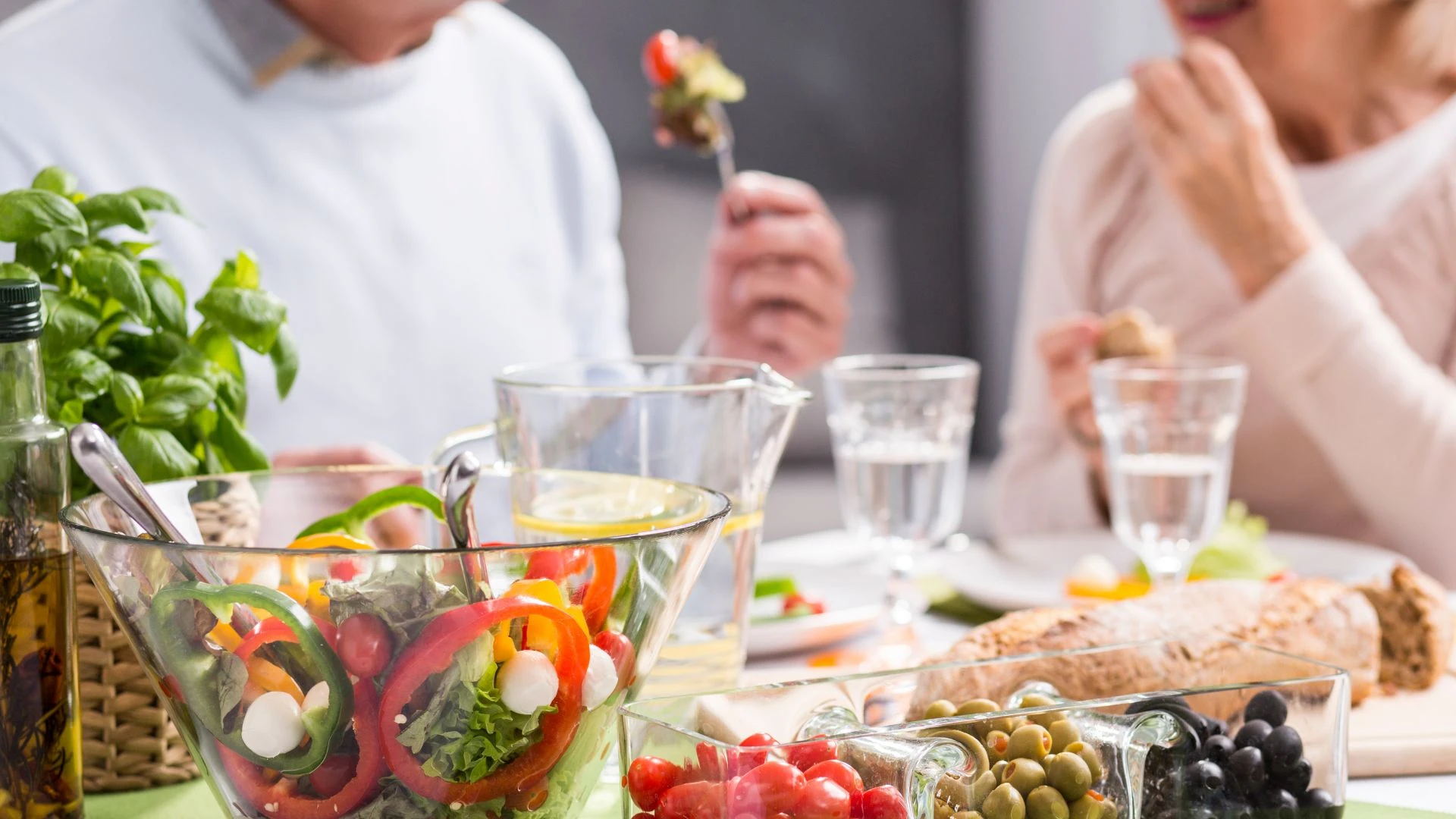 Zeytinyağlı sebzeler, tam tahıllar ve Akdeniz tipi salata eşliğinde sofrada yemek yiyen insanlar