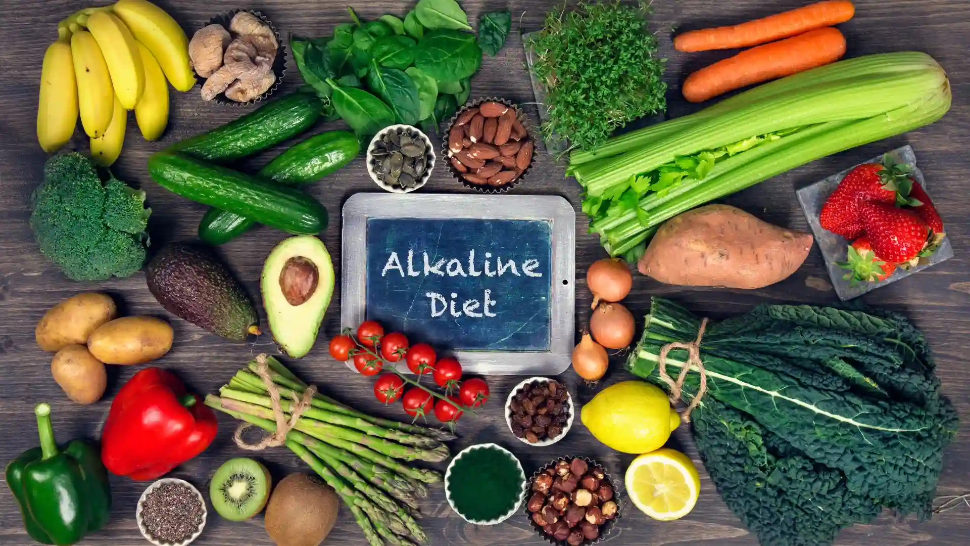 Üzerinde "Alkaline Diet" yazan bir tahta etrafında toplanmış brokoli, avokado, limon, kuşkonmaz ve kuruyemişlerden oluşan sağlıklı alkali besinler.
